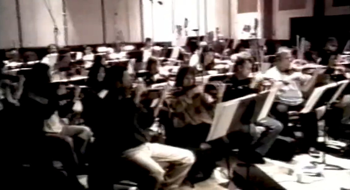 An orchestra recording in a large studio, in black and white